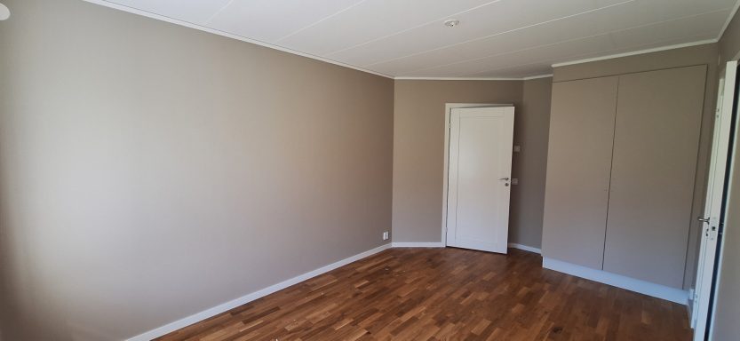 Vägg- & garderobs målning Tomt rum med beige väggar och trägolv, en dörr och en garderob syns på sidan.
