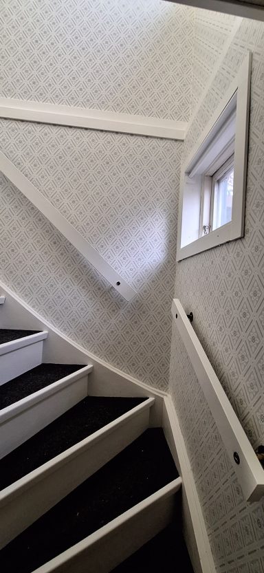 Tapetsering & Målning Trappa med svarta steg och vit vägg, fönster syns på övervåningen.
