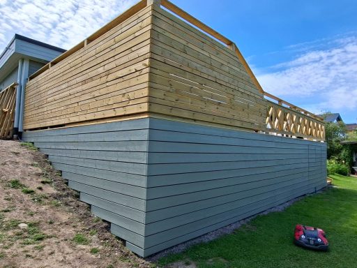 Altanbygge med nedsänkt SPA bad Husgavl med träpanel och grå stående brädor, gräsmatta i förgrunden.